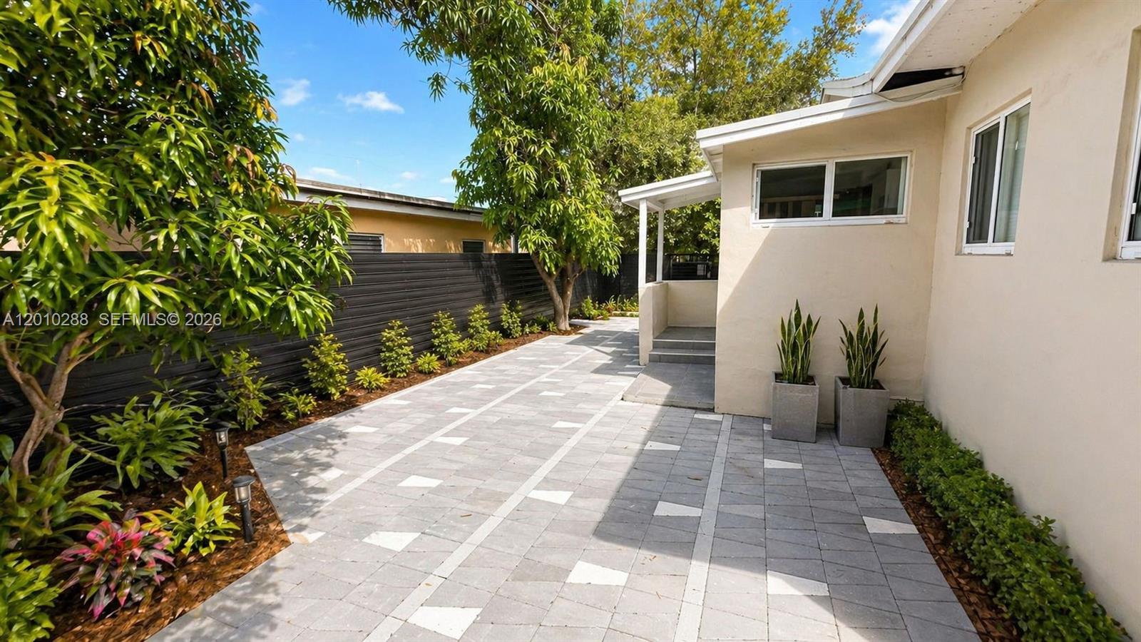 A paved patio area features a black fence, landscaping, and a covered building entrance — 135 NW 68th St, Miami FL 33150, MIAMI, FL