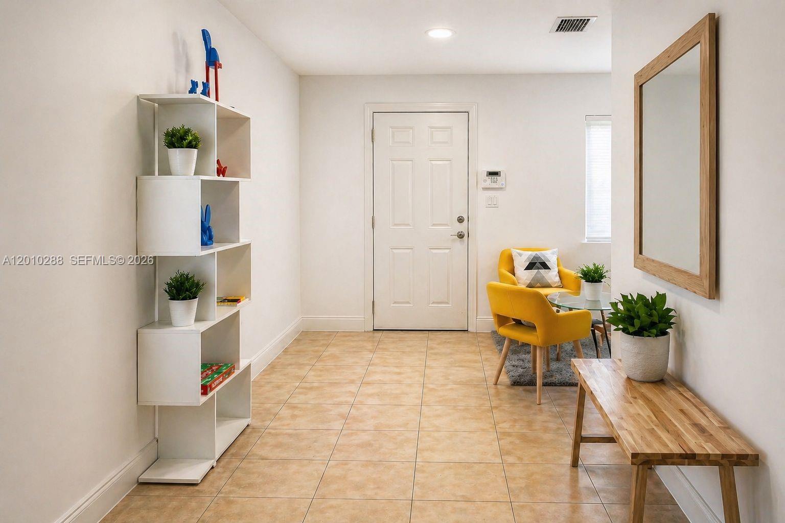 A bright entryway features a white bookshelf, yellow chairs, a wooden bench, and tile flooring — 135 NW 68th St, Miami FL 33150, MIAMI, FL