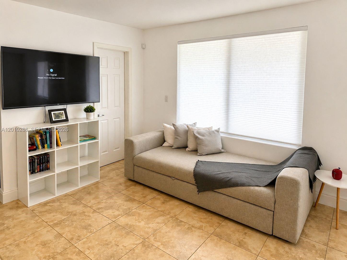 A living room features a sofa, a white bookshelf, a wall-mounted television, and tile flooring — 135 NW 68th St, Miami FL 33150, MIAMI, FL