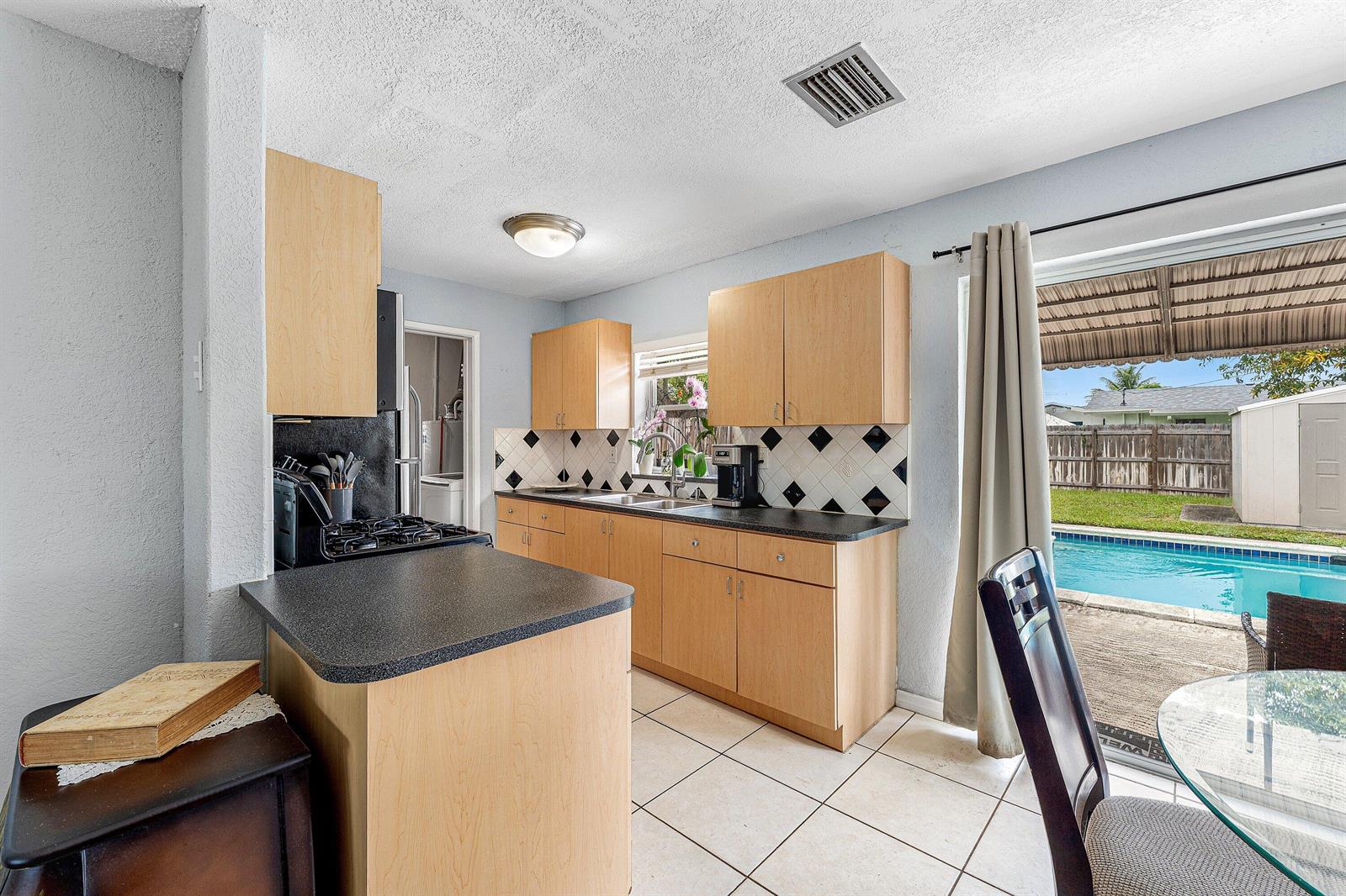 A kitchen with light wood cabinets, black countertops, and a sliding door to a pool — 5543 SW 7th Street, Margate FL 33068, MARGATE, FL