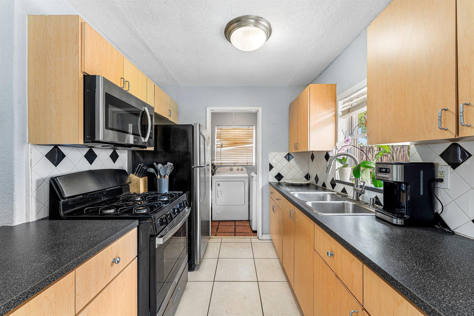 A galley kitchen features light wood cabinets, black countertops, a gas stove, and tiled floors — 5543 SW 7th Street, Margate FL 33068, MARGATE, FL