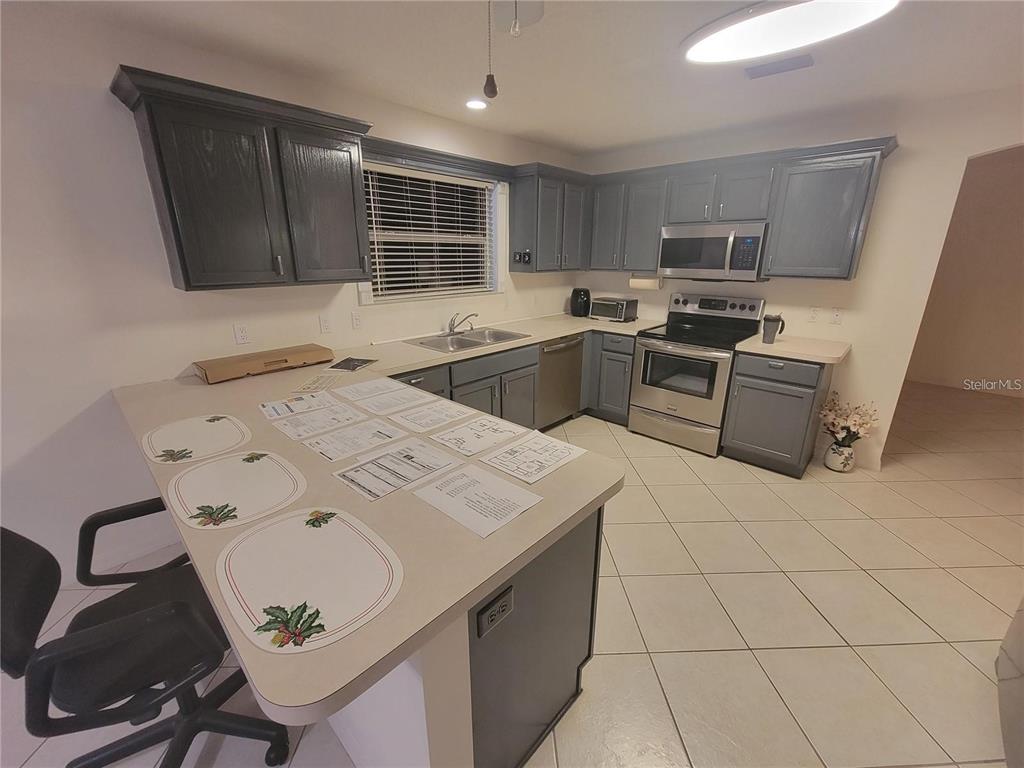 A kitchen with dark cabinets, light countertops, tile flooring, and an adjacent dining area — 1033 OAK FOREST DRIVE, THE VILLAGES, FL