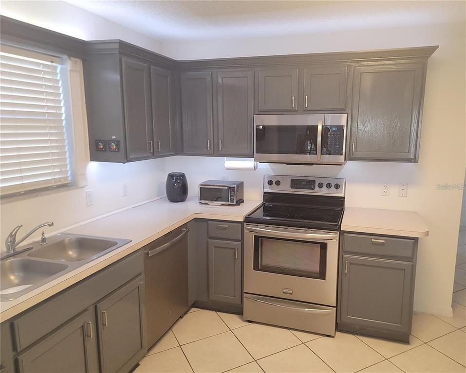 A kitchen features gray cabinets, stainless steel appliances, a peninsula counter, and tiled flooring — 1033 OAK FOREST DRIVE, THE VILLAGES, FL