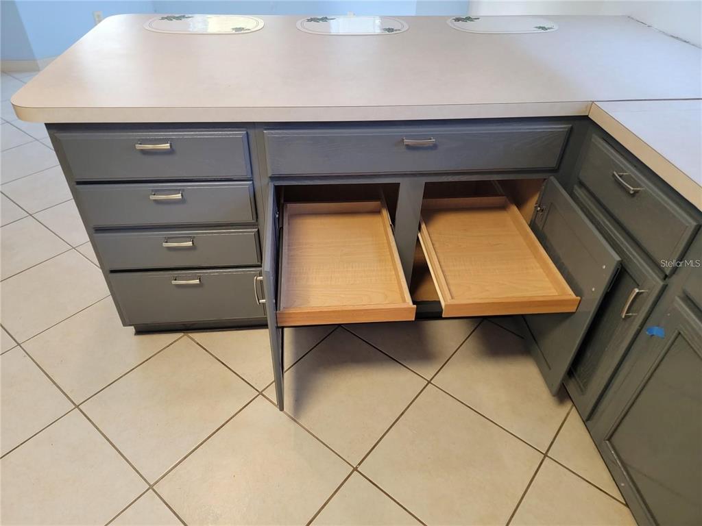 A kitchen features gray cabinets, stainless steel appliances, white countertops, and light-colored tile flooring — 1033 OAK FOREST DRIVE, THE VILLAGES, FL