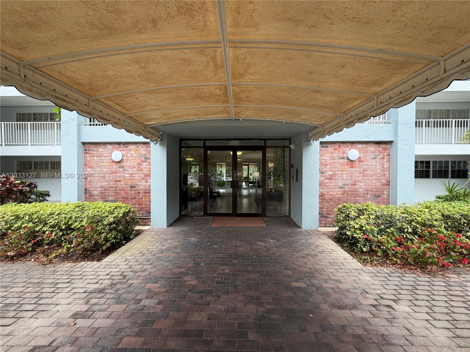 A brick walkway leads to the glass entrance doors of a building under a canopy — 3100 N Course Ln # 208, Pompano Beach FL 33069, POMPANO BEACH, FL
