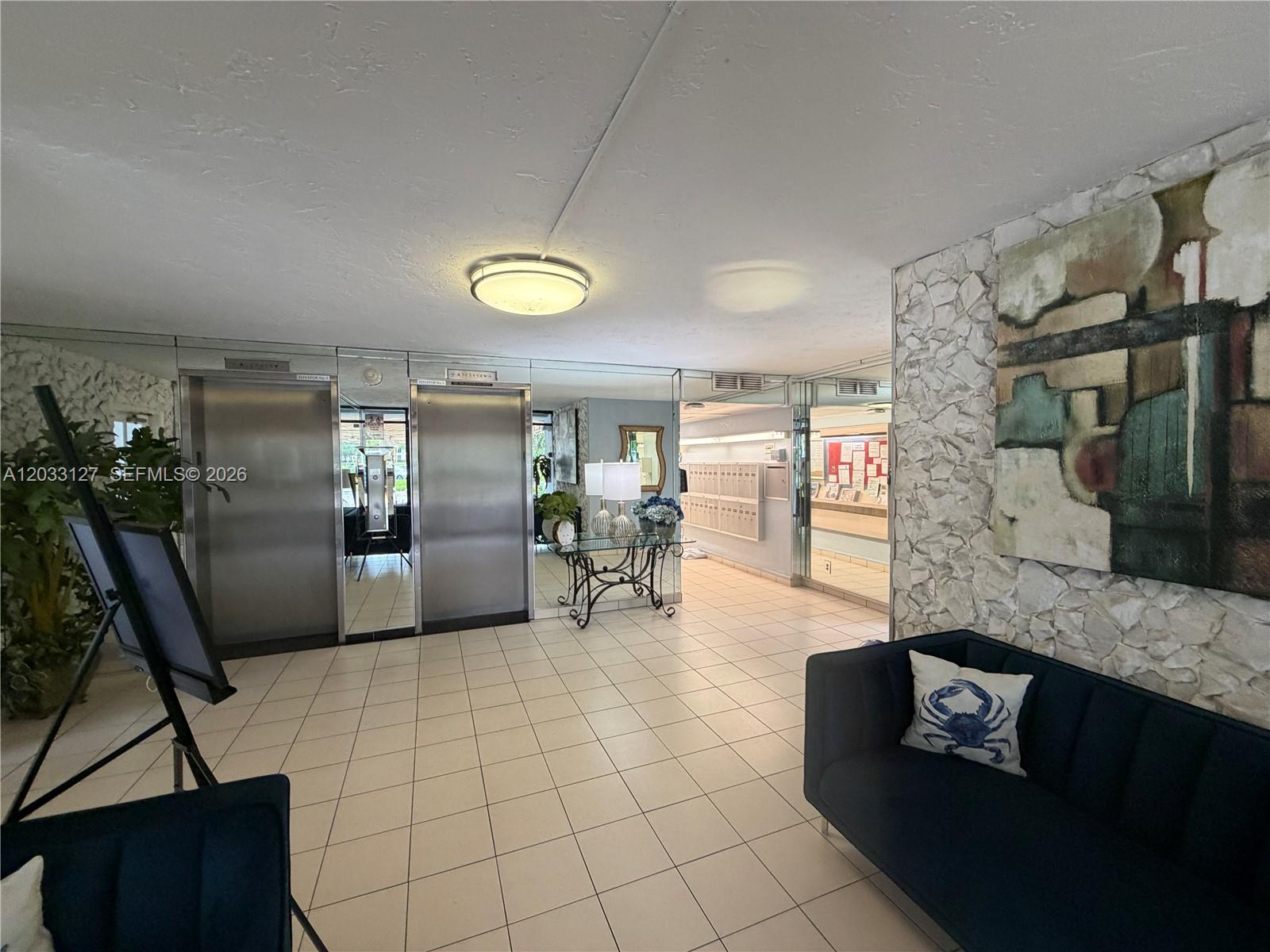 A lobby features tiled floors, two stainless steel elevators, a blue sofa, and stone walls — 3100 N Course Ln # 208, Pompano Beach FL 33069, POMPANO BEACH, FL