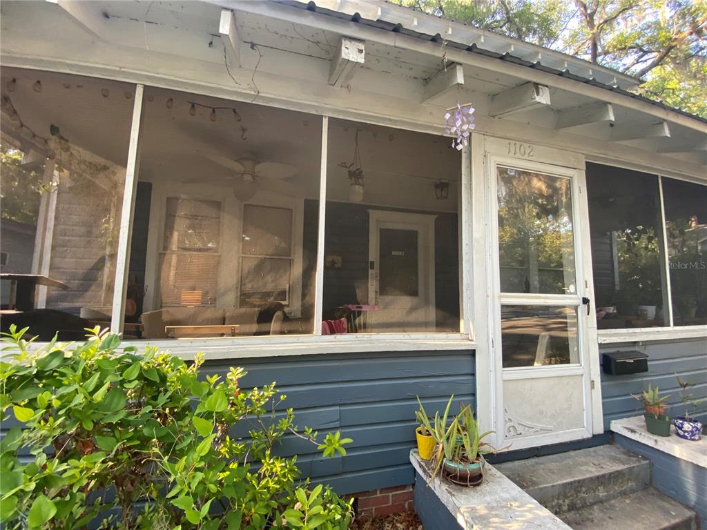 A screened-in front porch features blue horizontal siding, a white door, and potted plants — 1102 NW 3RD AVENUE, GAINESVILLE, FL