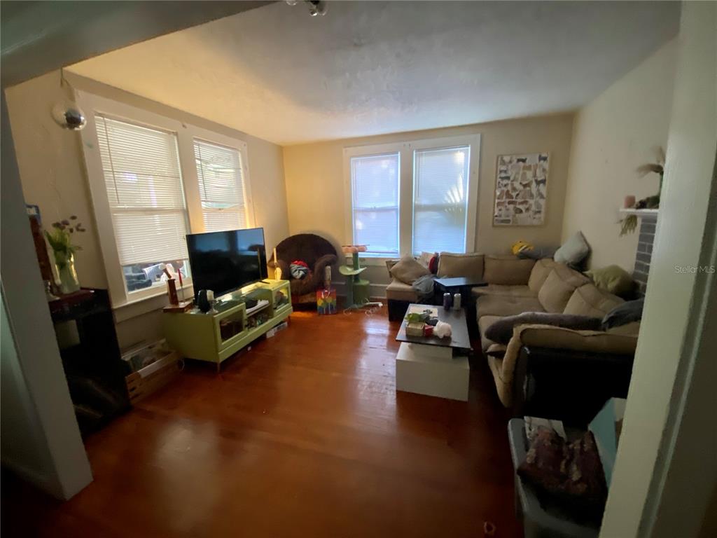 A living room features hardwood floors, a sectional sofa, a television on a stand, and windows — 1102 NW 3RD AVENUE, GAINESVILLE, FL