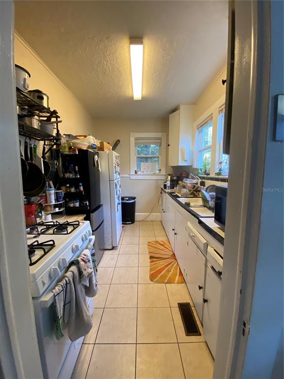 A narrow kitchen features white cabinets, a gas stove, a refrigerator, and tiled flooring — 1102 NW 3RD AVENUE, GAINESVILLE, FL