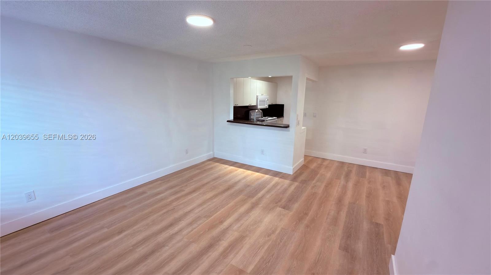 An empty room with light wood-look flooring features a pass-through opening to a kitchen — 2735 W 66th St # 23, Hialeah FL 33016, HIALEAH, FL