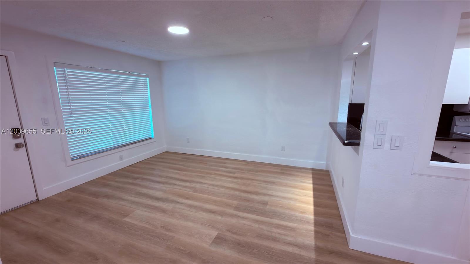 An empty room features light wood-look flooring, white walls, a window with blinds, and a pass-through — 2735 W 66th St # 23, Hialeah FL 33016, HIALEAH, FL