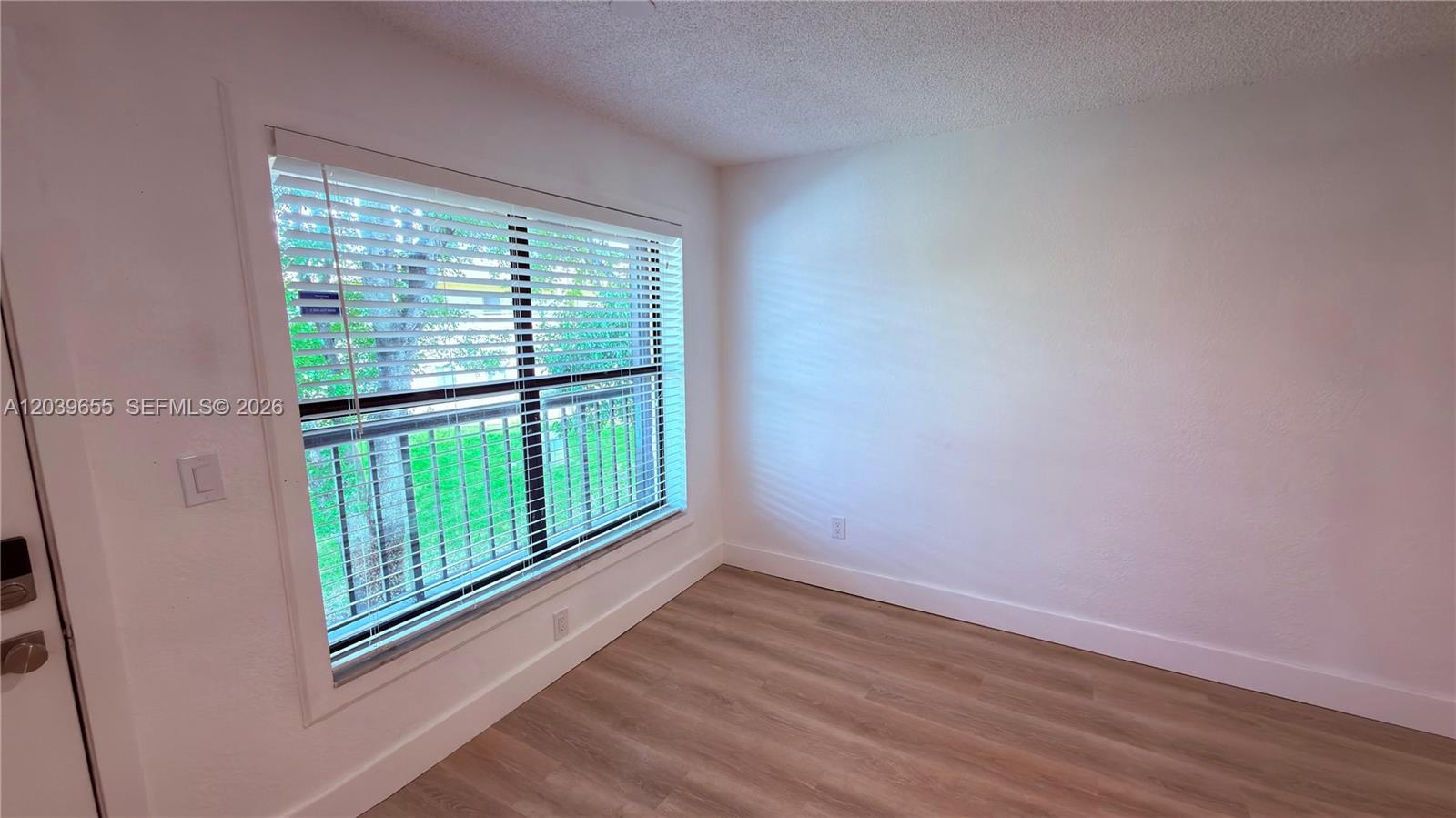 An empty room features light wood-look flooring, white walls, and a large window with blinds — 2735 W 66th St # 23, Hialeah FL 33016, HIALEAH, FL