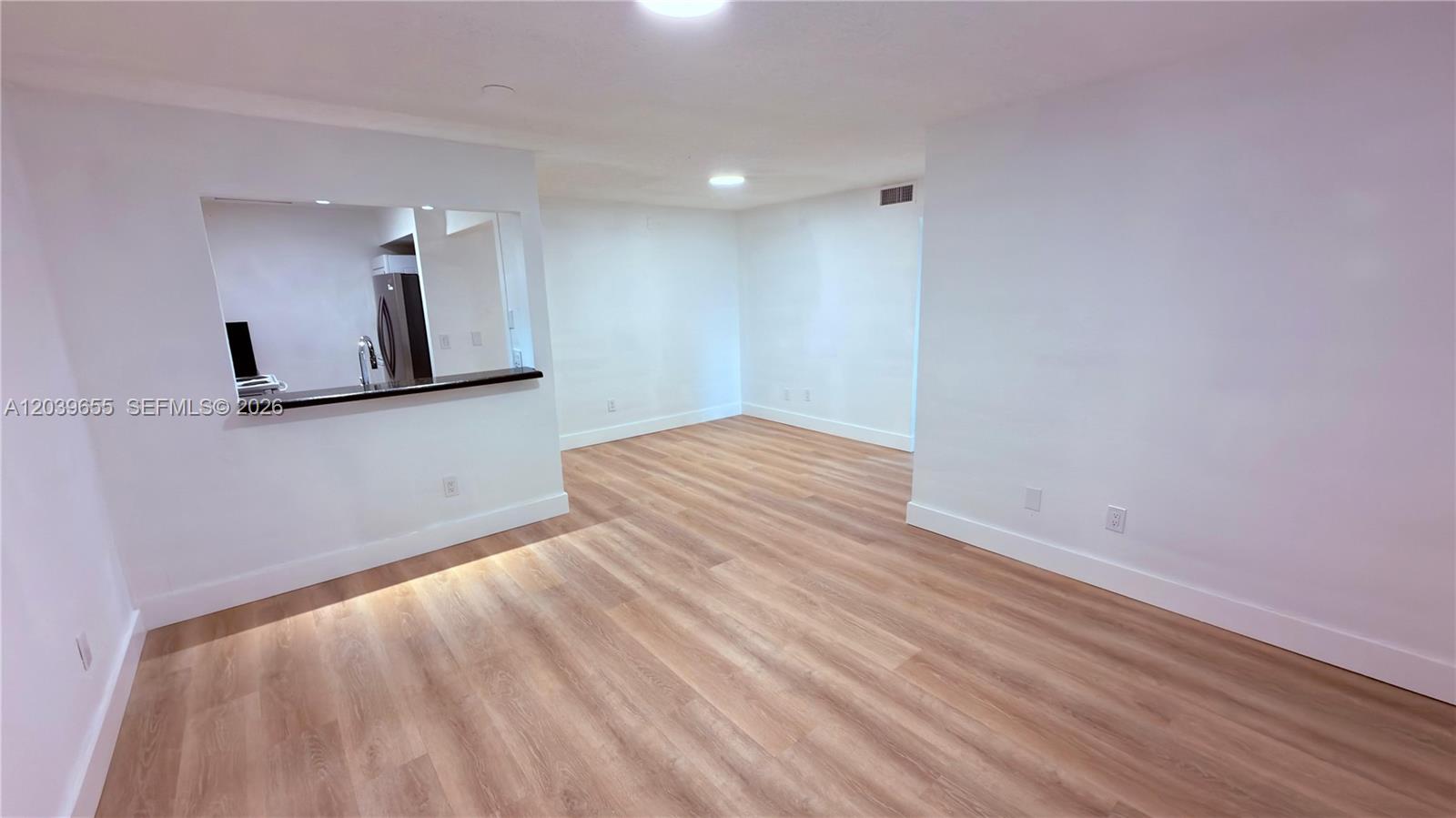 An empty room features light wood-look flooring, white walls, and a pass-through to a kitchen — 2735 W 66th St # 23, Hialeah FL 33016, HIALEAH, FL