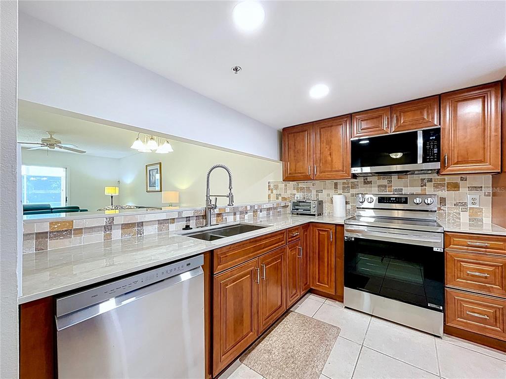 A kitchen with wood cabinets, stainless steel appliances, and a pass-through window to the living area — 7201 29TH AVE DRIVE UNIT 102, BRADENTON, FL