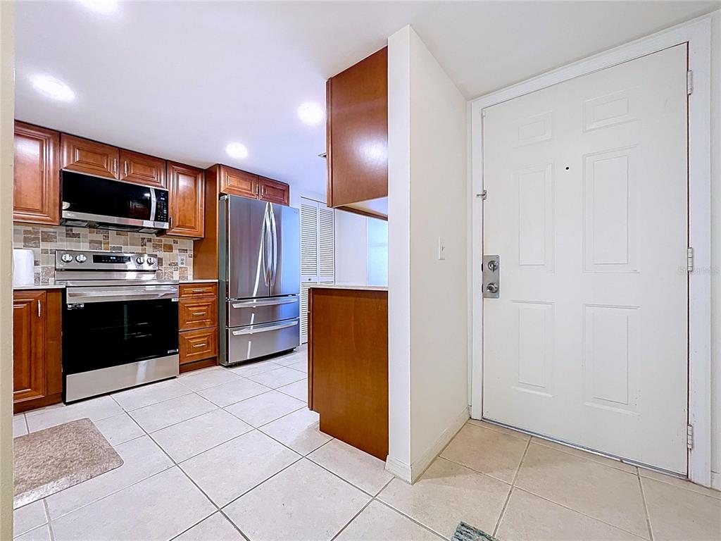A kitchen with wood cabinets, stainless steel appliances, and tile flooring next to an entryway — 7201 29TH AVE DRIVE UNIT 102, BRADENTON, FL