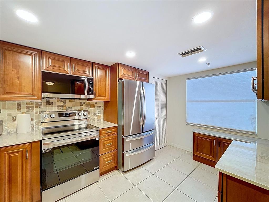A kitchen features wood cabinets, stainless steel appliances, a tiled backsplash, and light-colored floor tiles — 7201 29TH AVE DRIVE UNIT 102, BRADENTON, FL