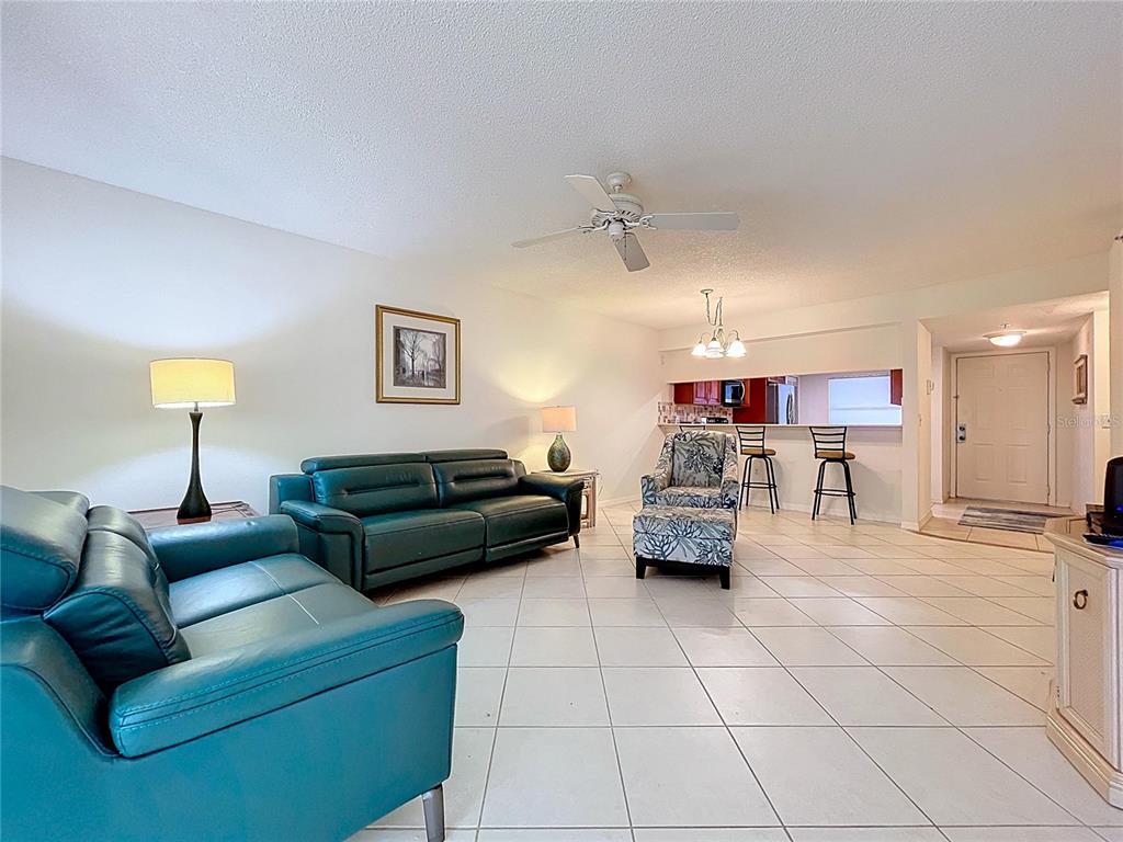 A living room with teal leather sofas, a patterned armchair, and tile flooring — 7201 29TH AVE DRIVE UNIT 102, BRADENTON, FL