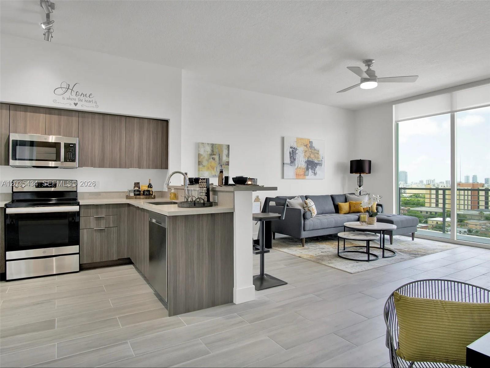 An open-concept kitchen and living area features wood-tone cabinetry, stainless steel appliances, and balcony access — 1000 NW 7th St # 710, Miami FL 33136, MIAMI, FL