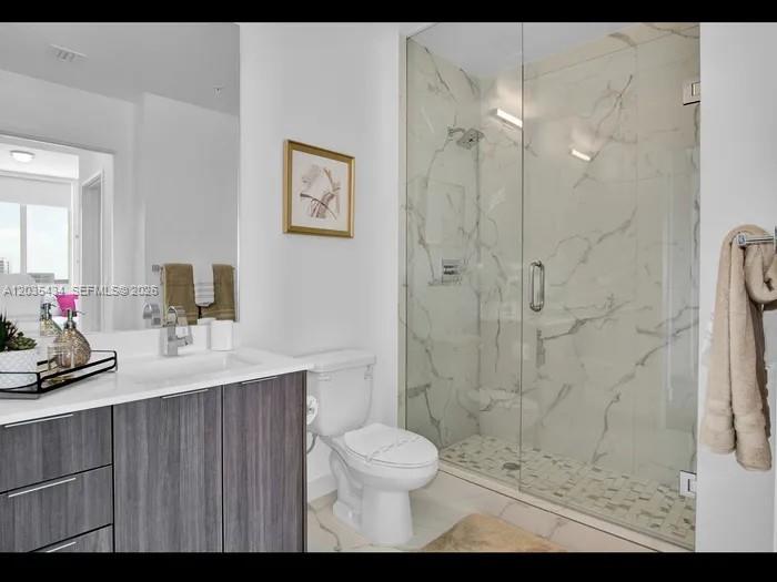 A modern bathroom features a wood-grain vanity, a white toilet, and a glass-enclosed marble shower — 1000 NW 7th St # 710, Miami FL 33136, MIAMI, FL