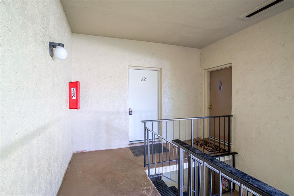 An outdoor apartment hallway features two numbered doors, a fire extinguisher, and a metal railing — 3236 S SEMORAN BOULEVARD UNIT 22, ORLANDO, FL