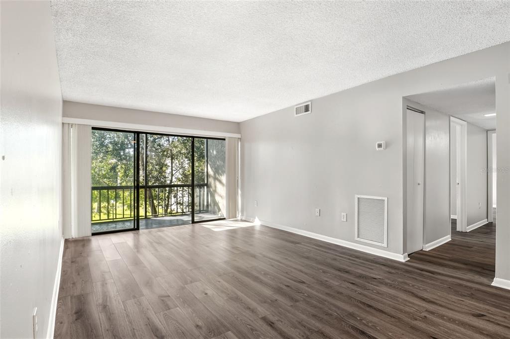 An empty living room features light gray walls, wood-look flooring, and a sliding glass door — 3236 S SEMORAN BOULEVARD UNIT 22, ORLANDO, FL