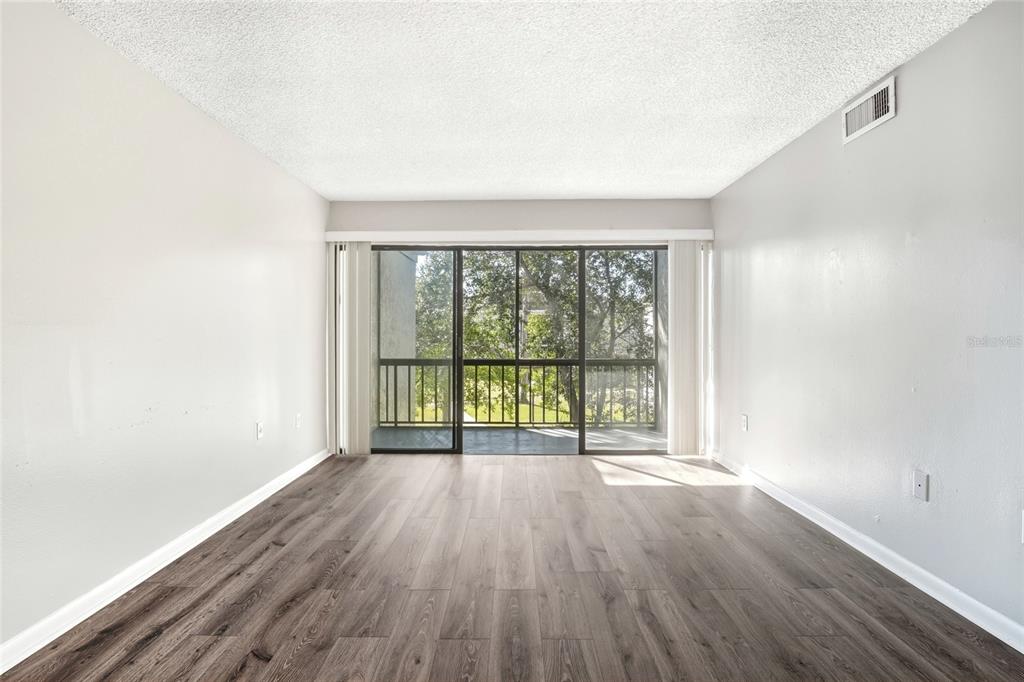 An empty living room features light gray walls, wood-look flooring, and a sliding glass door — 3236 S SEMORAN BOULEVARD UNIT 22, ORLANDO, FL