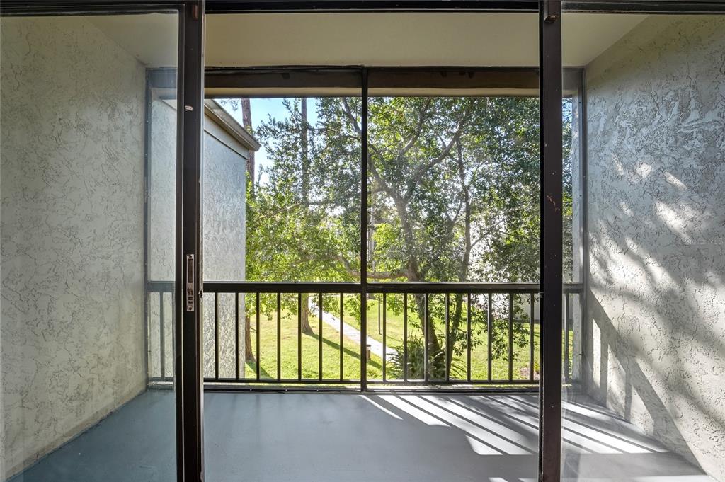 A screened-in balcony with a concrete floor and sliding glass doors overlooking a grassy area — 3236 S SEMORAN BOULEVARD UNIT 22, ORLANDO, FL