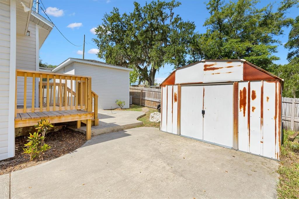 A backyard view showing a wooden deck, a concrete patio, and a weathered metal shed — 2000 SOUTH STREET, LEESBURG, FL