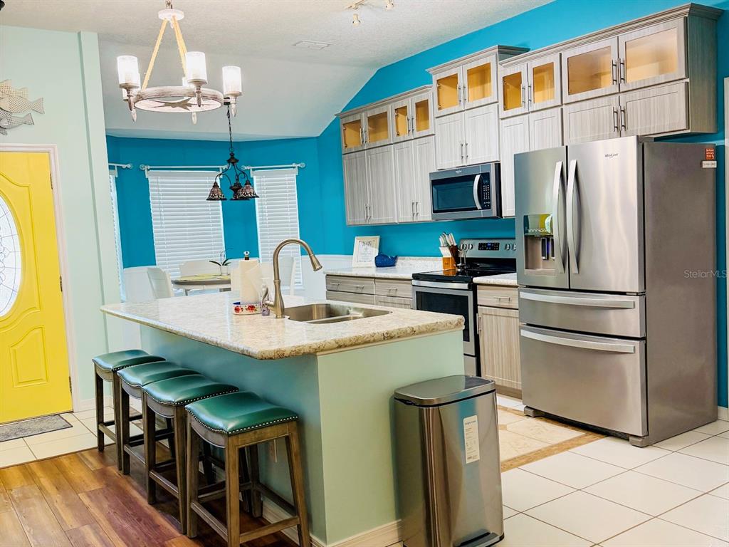 A kitchen features a central island, stainless steel appliances, light wood cabinets, and turquoise walls — 1580 DORSET DRIVE, MOUNT DORA, FL