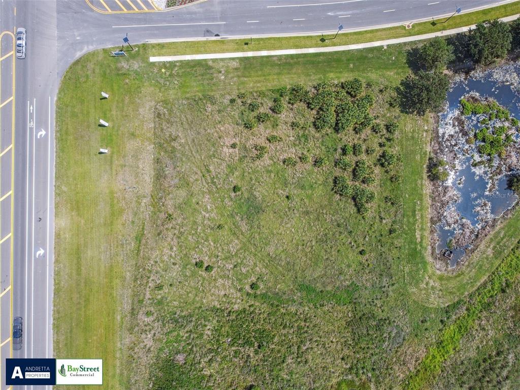 An aerial view shows a vacant, grassy corner lot bordered by a road and a pond — 0 N GALL BOULEVARD UNIT 1.08 Acres, ZEPHYRHILLS, FL