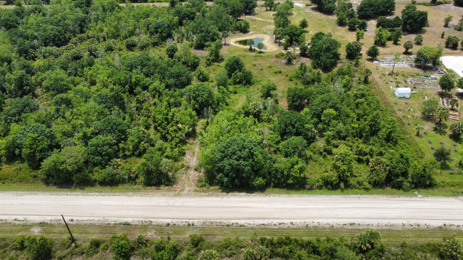 An aerial view shows a dirt road bordering a wooded lot with a small pond — 16436 NW 256th Street, Okeechobee FL 34972, OKEECHOBEE, FL