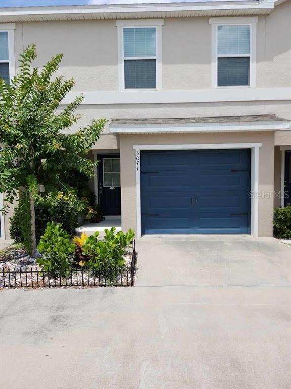 A two-story townhouse exterior features a blue garage door, a front entrance, and landscaping — 3071 FIELDWOOD CIRCLE, ST CLOUD, FL