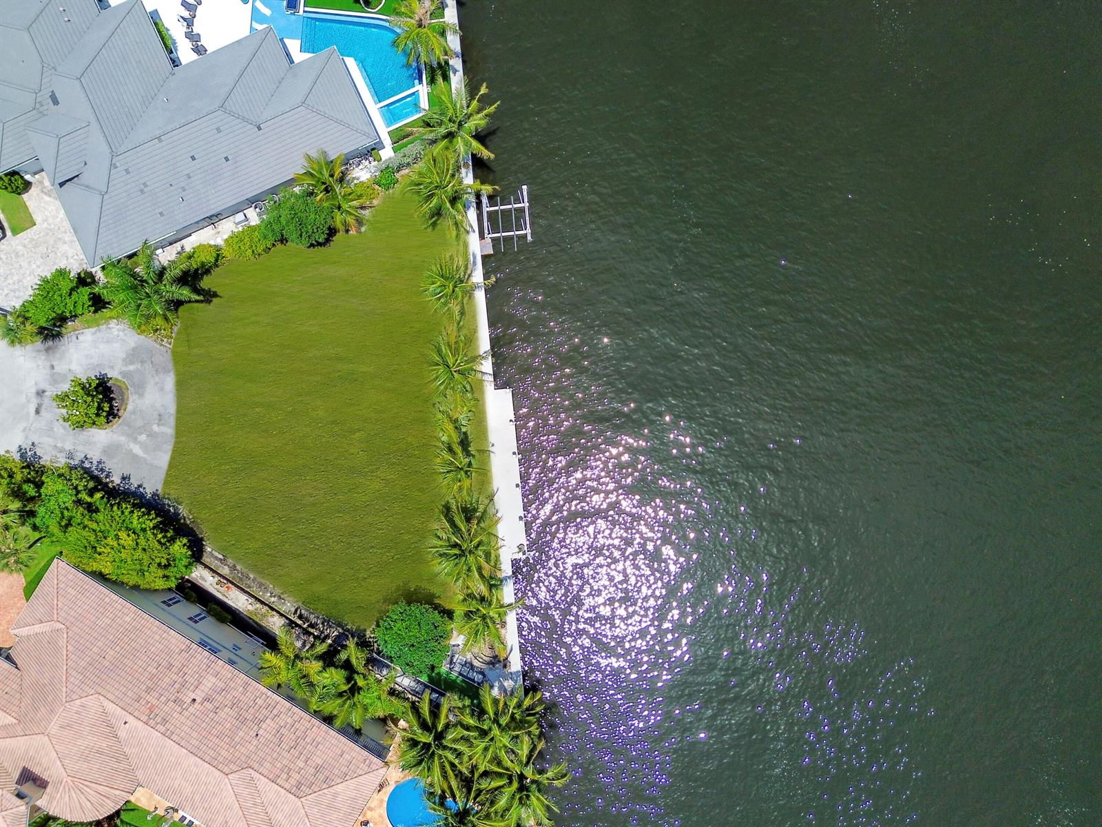 An aerial view shows a waterfront property with a large lawn, swimming pool, and dock — 976 Banyan Drive, Delray Beach FL 33483, DELRAY BEACH, FL