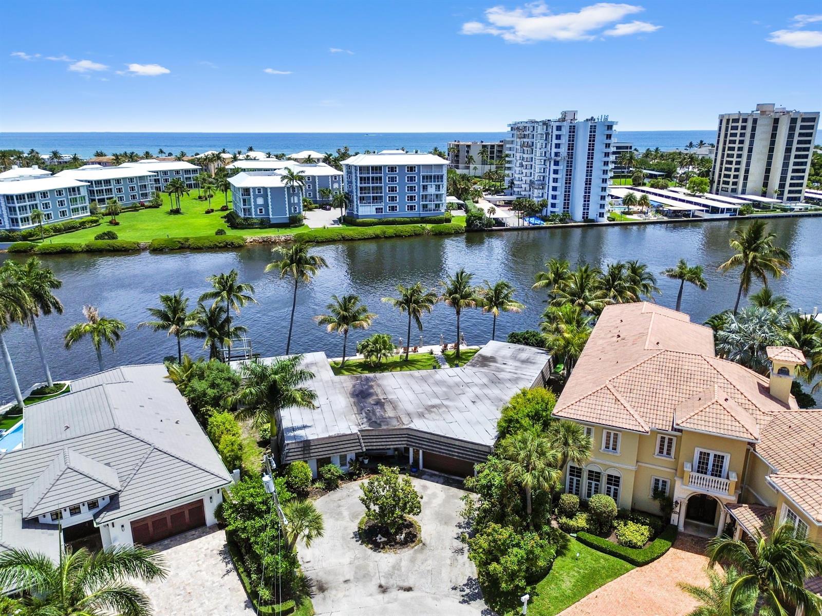 An aerial view shows waterfront homes with palm trees, a canal, and distant apartment buildings — 976 Banyan Drive, Delray Beach FL 33483, DELRAY BEACH, FL
