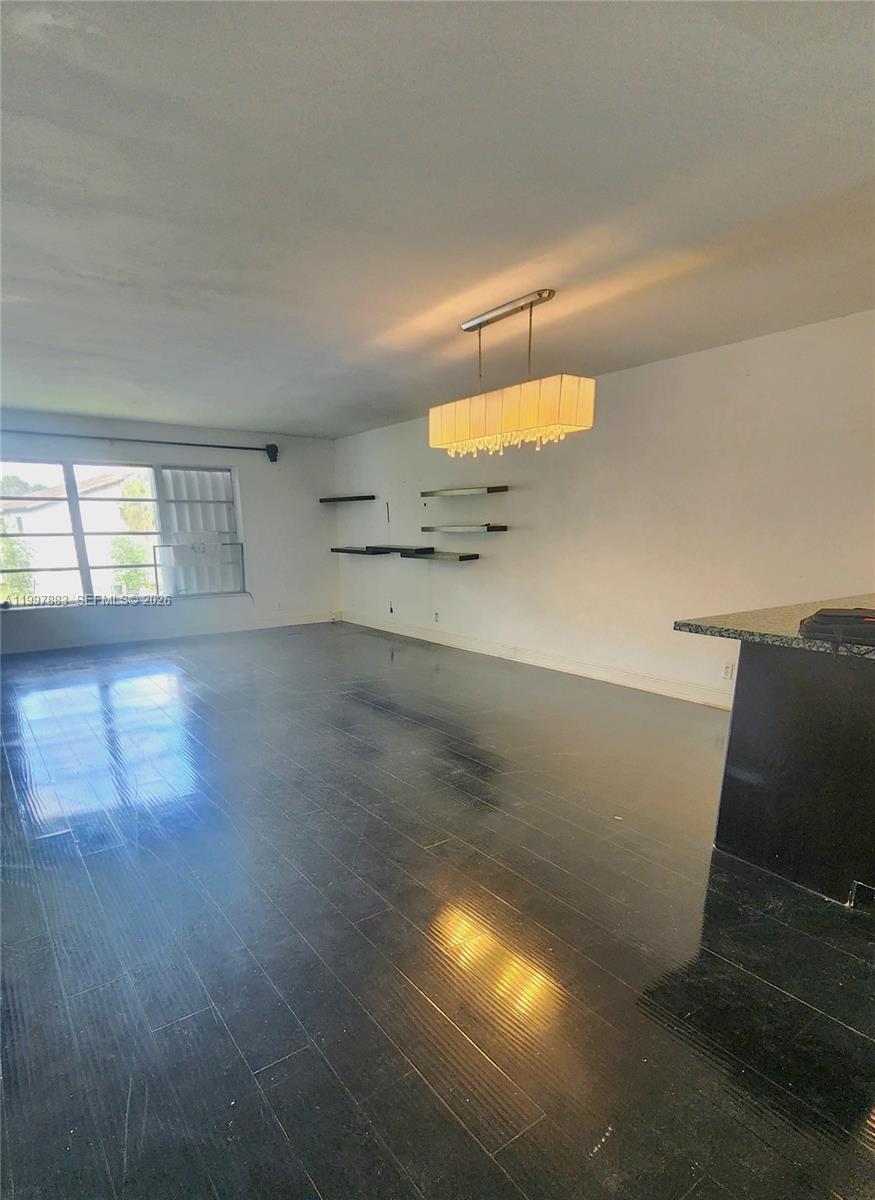 An empty room features dark wood flooring, white walls, and a hanging chandelier — 3811 NW 84th Ave # 2B, Sunrise FL 33351, SUNRISE, FL