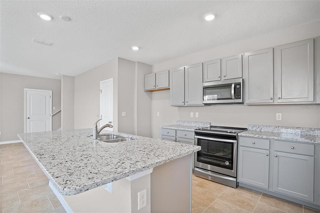 A kitchen features gray cabinets, granite countertops, a stainless steel oven, and a center island — 11092 GREAT ROCK STREET, WINTER GARDEN, FL