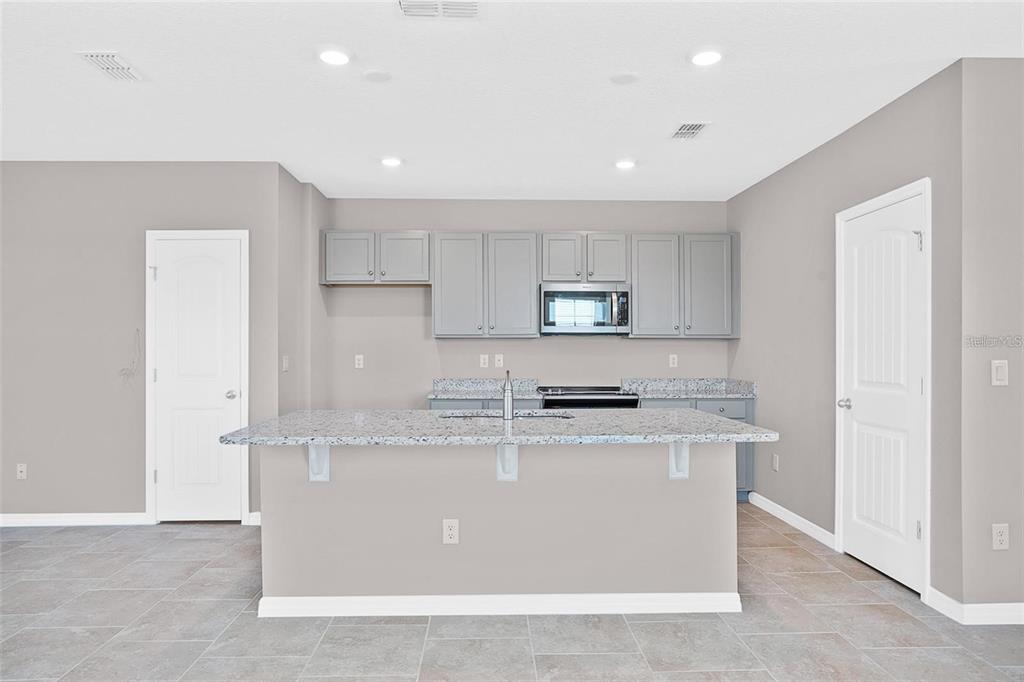 A kitchen features gray cabinets, granite countertops, a central island, and light-colored tile flooring — 11092 GREAT ROCK STREET, WINTER GARDEN, FL