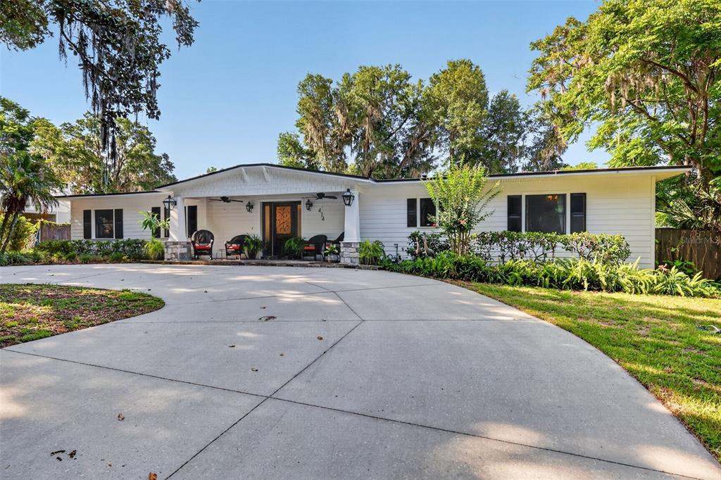 A white single-story house with a large concrete driveway and a covered front porch — 414 W 12TH AVENUE, MOUNT DORA, FL