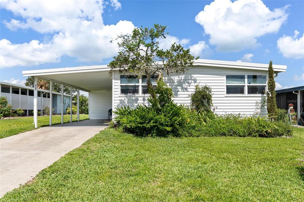 A single-story white house with a carport and a front lawn under a blue sky — 717 W COACH N FOUR DRIVE, LEESBURG, FL