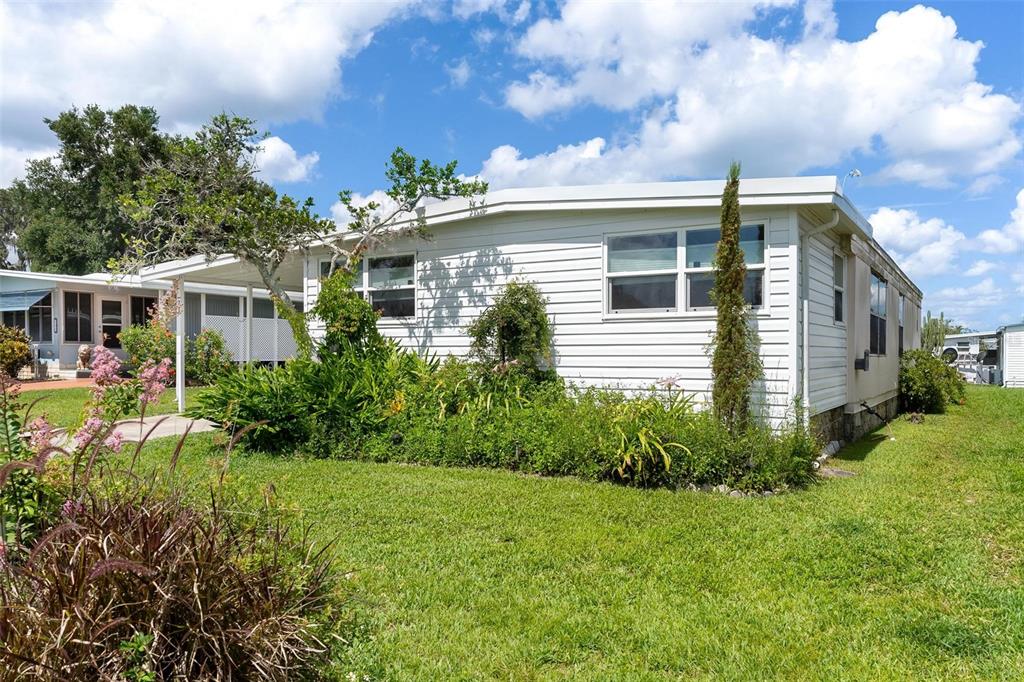A white single-wide mobile home with a covered porch and landscaping under a blue sky — 717 W COACH N FOUR DRIVE, LEESBURG, FL