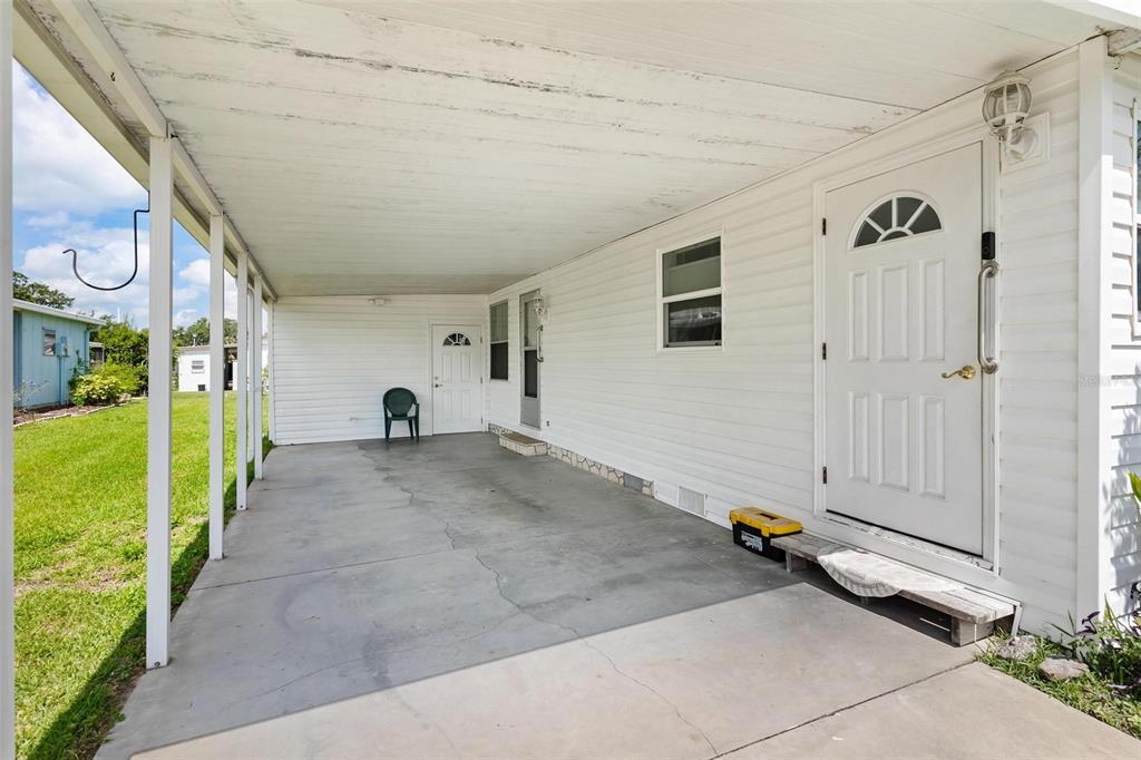 A covered concrete carport area features white siding, two exterior doors, and a single window — 717 W COACH N FOUR DRIVE, LEESBURG, FL