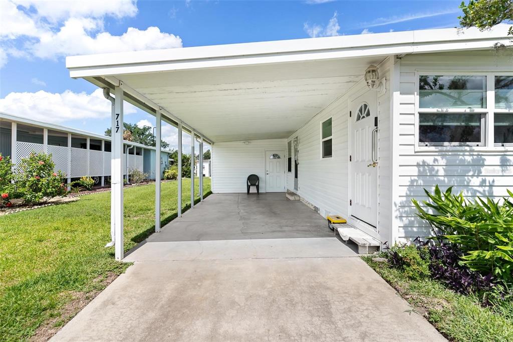 A white mobile home exterior features a concrete carport and a front entrance door — 717 W COACH N FOUR DRIVE, LEESBURG, FL