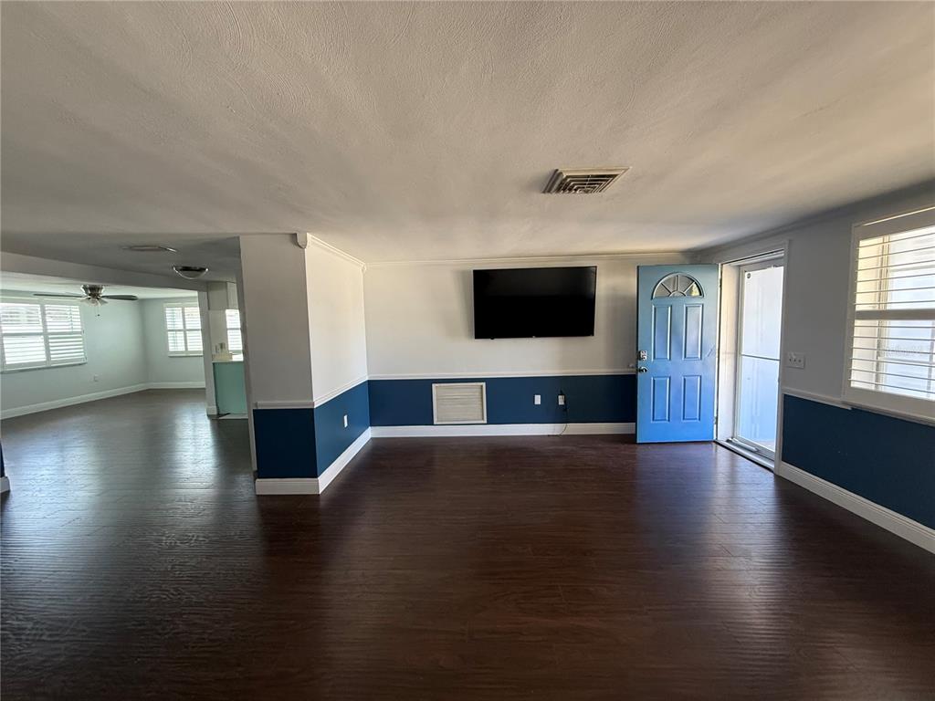 A living room features dark wood flooring, blue wainscoting, a wall-mounted television, and a blue door — 5240 SCHOOL ROAD, NEW PORT RICHEY, FL