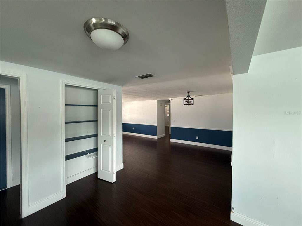 An interior view shows a room with dark wood flooring, white walls, and a pantry closet — 5240 SCHOOL ROAD, NEW PORT RICHEY, FL