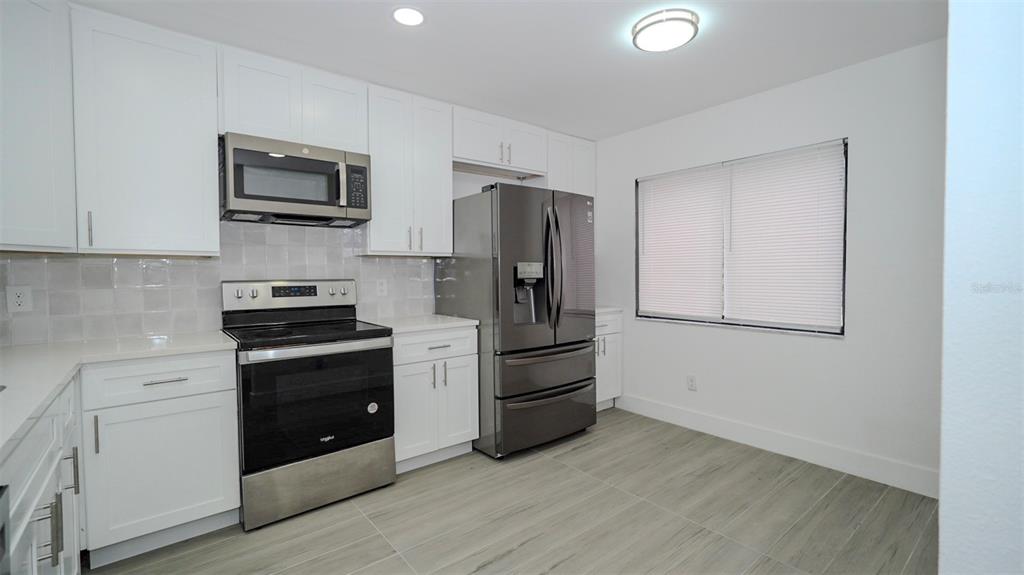A kitchen features white cabinets, stainless steel appliances, a tiled backsplash, and light-colored tile flooring — 4368 S LAKE ORLANDO PARKWAY UNIT 203, ORLANDO, FL