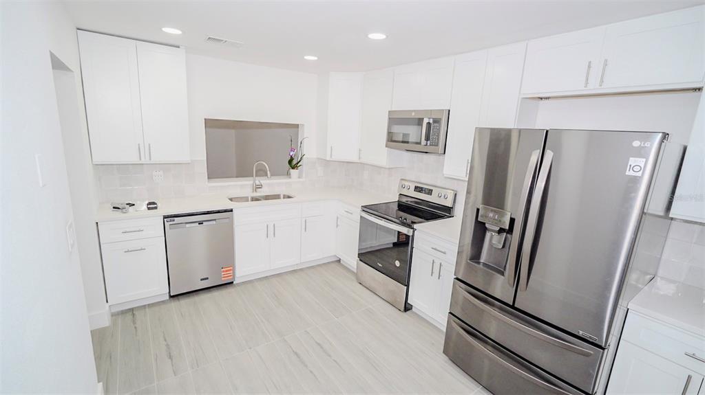 A modern kitchen features white cabinetry, stainless steel appliances, and light-colored tile flooring — 4368 S LAKE ORLANDO PARKWAY UNIT 203, ORLANDO, FL