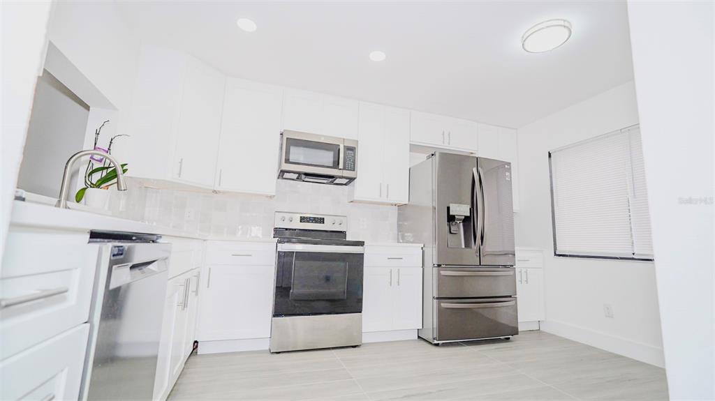 A modern kitchen features white cabinetry, stainless steel appliances, and light-colored tile flooring — 4368 S LAKE ORLANDO PARKWAY UNIT 203, ORLANDO, FL