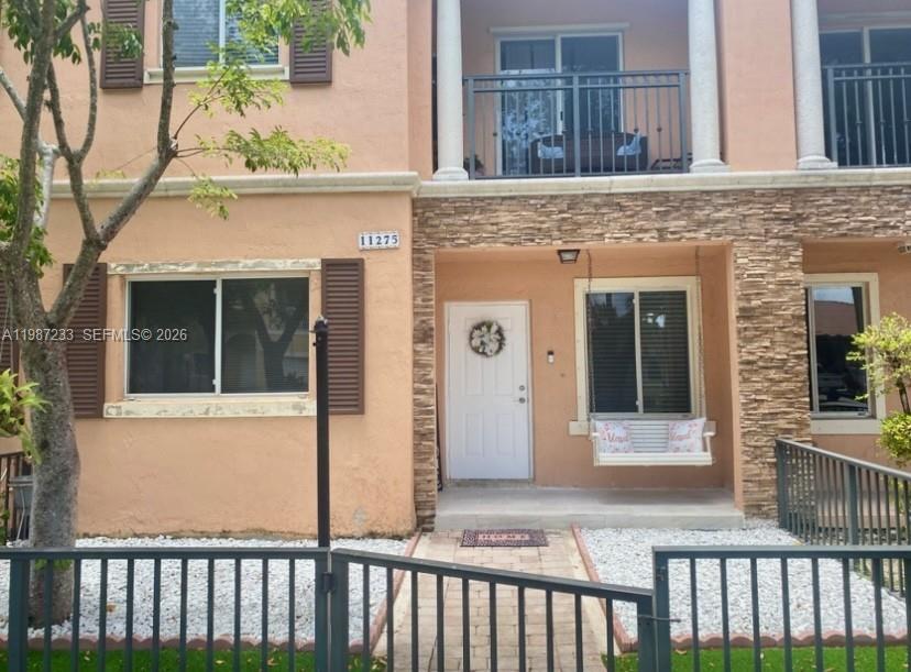 A two-story townhouse exterior features a white front door, a porch swing, and stone accents — 11275 SW 231st Ln, Miami FL 33170, MIAMI, FL