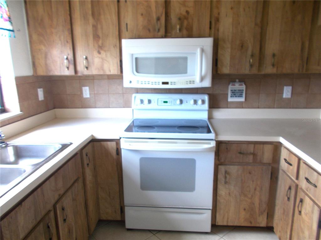 A kitchen features wood cabinets, white appliances, a tiled backsplash, and light-colored countertops — 2000 FORREST NELSON BOULEVARD UNIT C6, PORT CHARLOTTE, FL