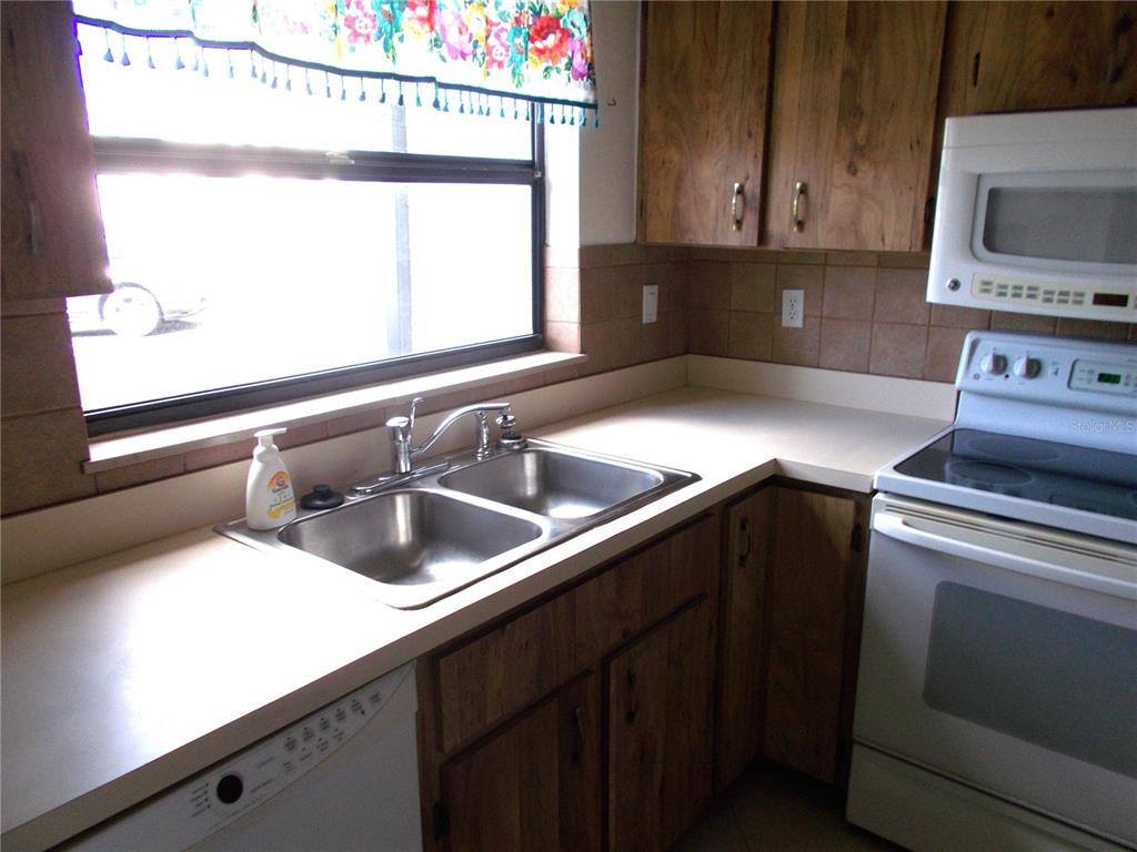 A kitchen features wood cabinets, a double-basin sink, white appliances, and a window with curtains — 2000 FORREST NELSON BOULEVARD UNIT C6, PORT CHARLOTTE, FL